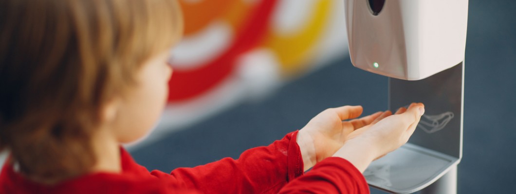 copil care tine mainile sub dozator pentru dezinfectant de maini la scoala